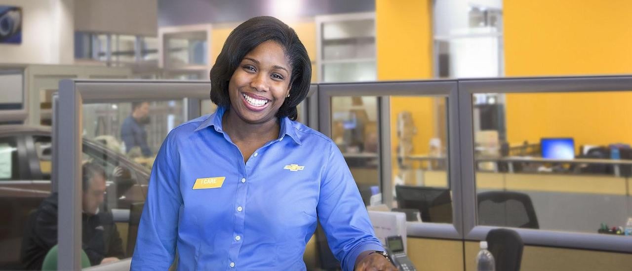Woman smiling wearing a blue shirt with the Chevrolet logo on the chest and a name tag that reads 'I care'