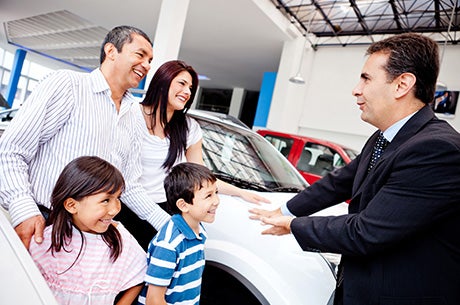 Family talking to a salesman in front of a white car